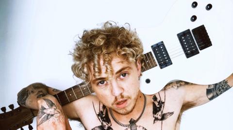 A photo of a topless man with a guitar