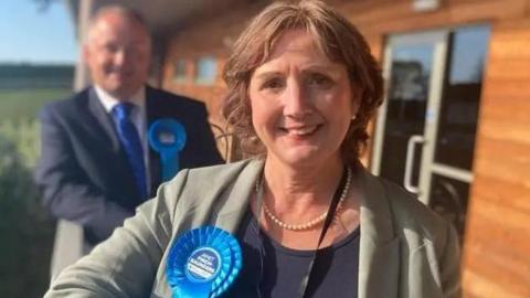 Janet Finch-Saunders smiling with a blue rosette attached to her lapel. 