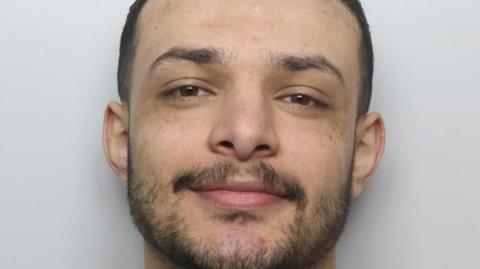 Custody picture of a man with a short beard smiling.