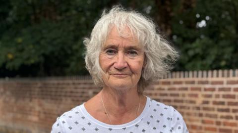 A woman in a white T-shirt with small black motif designs. She has jaw length grey hair
