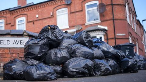 Pile of bin bags outside red brick houses