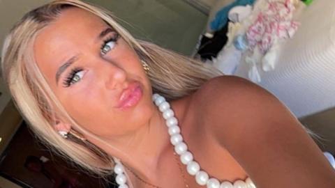 Chloe Watson Dransfield is pictured looking directly at the camera and pouting. She has long, blonde hair and is wearing a white top with beading around the neck line.