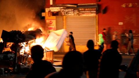 A man throws an item onto a fire during unrest in Harehills, Leeds