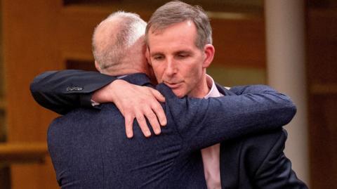 Two men in suits hugging.