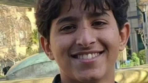 Abdullah looks into the camera with a smile showing his teeth. He has short dark hair.