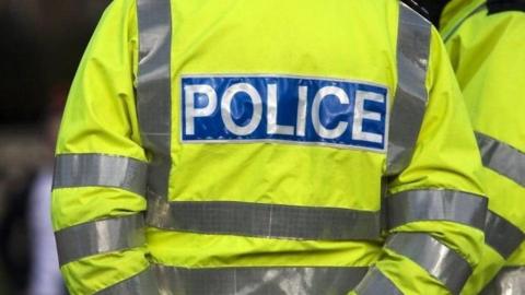 A police officer wearing a neon yellow hi-vis vest with the word "police" in white letters on a blue background on the back 