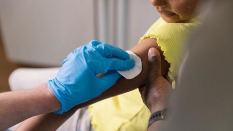 A children getting their arm swabbed with a cotton pad before an injection