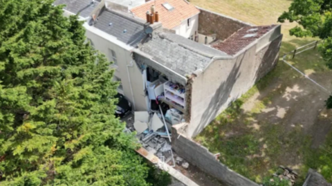 A picture of a house that was damaged in an explosion. There is a property with part of the back wall missing across two storeys and plaster spread everywhere.