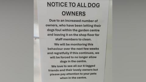 A white sign with black writing which has been displayed in the garden centre. The top of the sign reads 'Notice to all dog owners'.