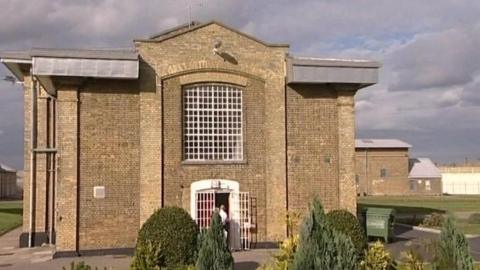 A prison building with large windows with metal bars in front of them.