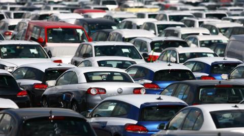 A large amount of cars all lined up. All you can see are cars parked very closely together. All number plates are not visible and all the cars appear to be parked with nobody in them.