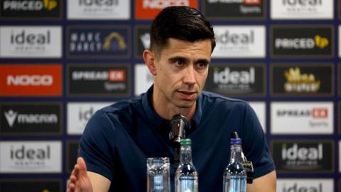 New West Bromwich Albion head coach Eric Ramsay sits in front of a microphone and water bottles at his first press conference as boss