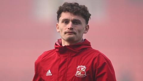 Swindon Town defender Billy Kirkman wearing a red training top with the Swindon Town and adidas logos during the warm-up for a League Two football match.