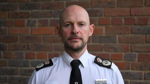 Jason Hogg, dressed in police uniform, stood in front of a brick wall.