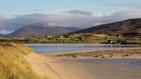 A view of a beach, loch, hills and houses in the Western Isles.