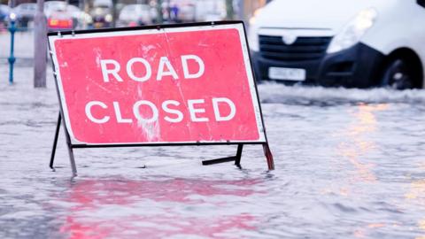 A generic image of a road closed sign on a flooded road