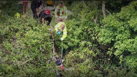 A fire and rescue team lower a rope to a casualty in a heavily overgrown area of West Sussex.