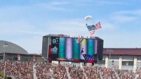 The skydiver begins his descent into the Virginia tech scoreboard.