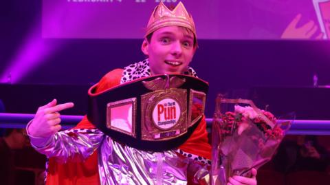 Adam Ernest Pickard bathed in purple light with a boxing-style belt around his shoulders