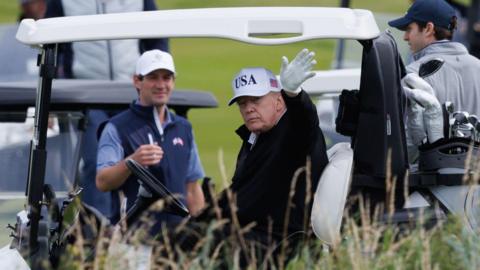Donald Trump waves to onlookers from his golf buggy