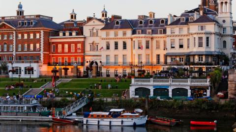 A row of buildings in front of a stepped lawn leading down to the River Thames.