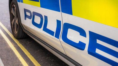 A stock image of the side of a police car, parked on double yellow lines.