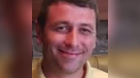 Tony Ferns smiles at the camera, wearing a yellow poloshirt. He has short brown hair and is sitting at what appears to be a booth in a bar or restaurant.