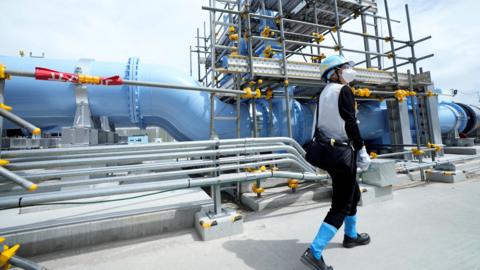 Man walks past a pipeline at the Fukushima Daiichi nuclear power plant