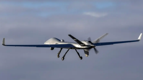 A generic image of a RAF surveillance drone flying in the sky with grey clouds behind it.