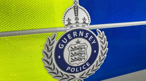 A fluorescent yellow and blue side of a Guernsey Police car with a coat of arms in the centre.