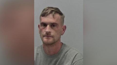 West Mercia Police mugshot of Mark Hirons. He is looking at the camera and has short dark blonde hair, and is wearing a grey T-shirt.