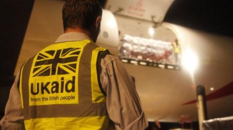 UK aid worker in front of a plane