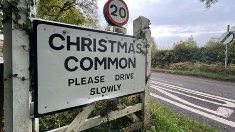 A roadsign alongside a road, saying "Christmas Common Please Drive Slowly"