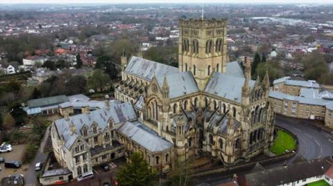 A drone image of the Roman Catholic Cathedral of St John the Baptist. It is a stone-built Victorian gothic-style building. The Norwich skyline can be seen in the background