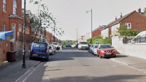 A street view of Cardinal Street. There are red-brick houses lining both sides of the road, and cars parked on the pavements.