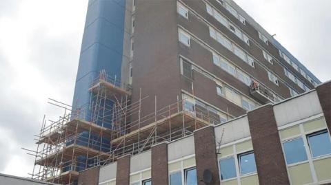 A University Hospital of North Tees building which is surrounded by scaffolding. The building is bricked and has very dated panels.