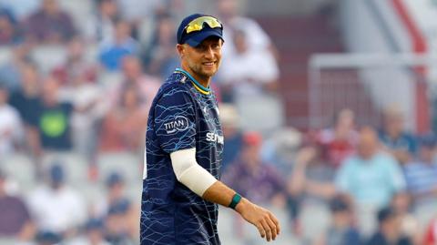 Joe Root in a blue Yorkshire top and cap with sunglasses on his head facing the camera while fielding in a T20 Blast match