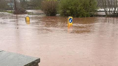 Flooded roads outside the Vine Tree pub in Crickhowell. You can see road sign markings sticking out from the middle of the road emphasising how the deep the water is. They are half covered,