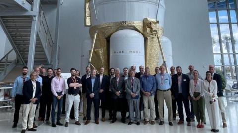 A delegation of space industry representatives standing in front of a Blue Moon lunar lander. The large craft is white with sections painted gold.