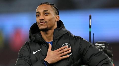 Joao Pedro pats the Chelsea badge while facing towards chanting fans