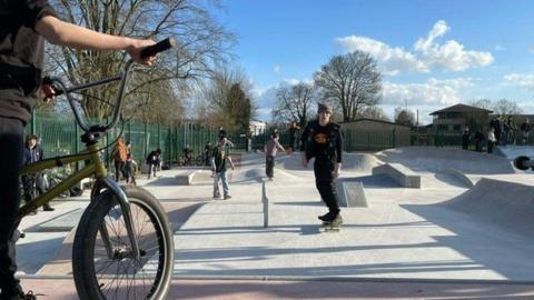 A skate park where a few young adults are riding skateboards and bikes on a sunny day