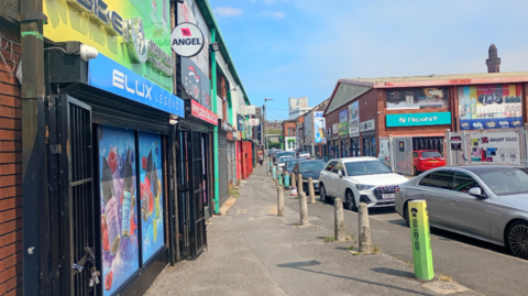 A row of vape shops in Harris Street with white and grey cars parked on it