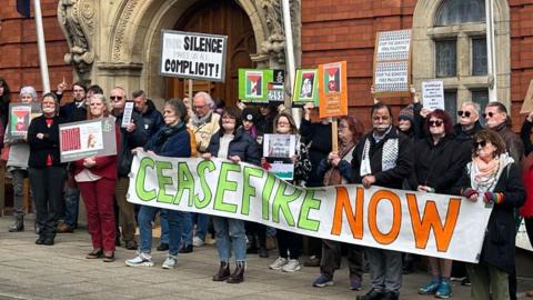 Demonstrators outside Tynwald with signs and tape over their mouths