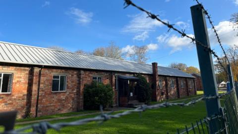A red-bricked military building. Barbed wire is in front of it.