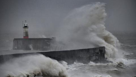 A large wave breaks over a harbour wall