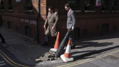 Men walking past a damaged pavement