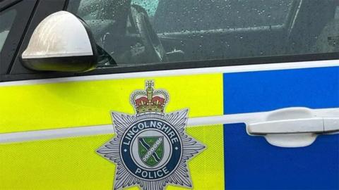 The side of a yellow and blue marked Lincolnshire Police car showing the force's badge