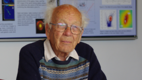 Sir Francis Graham-Smith, pictured in his 90s  in 2014. He has white hair on the sides of his head which is bald on top. He smiles at the camera. He wears glasses and a patterned jumper over a white open-necked shirt.
