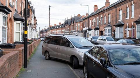 A residential street in Birmingham showing a silver car partially parked on the pavement 
