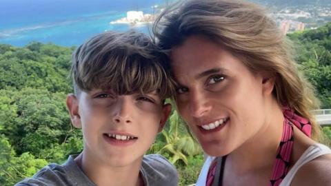 Jools and Ellen smile in a selfie. They are high lookout above a viewpoint, with lots of trees and a beach below. They are both smiling at the camera.